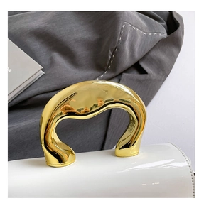Detail showing the white patent leather texture and organic gold metal handle of the bag