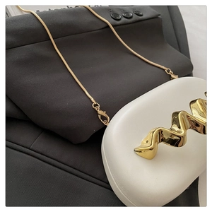 Detail of white acrylic clutch with wavy gold handle and sleek snake chain strap