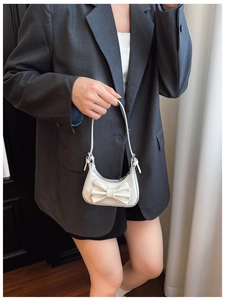 Détail du sac croissant blanc verni avec grand nœud et fermeture zippée sur modèle