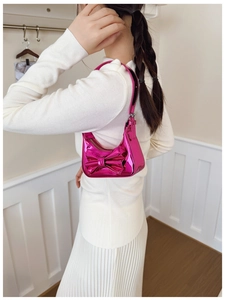 Détail du sac hobo fuchsia métallisé avec grand nœud porté par un mannequin en fond neutre