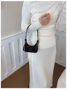 Détail d'un mini sac à bandoulière en cuir verni noir avec nœud porté comme accessoire