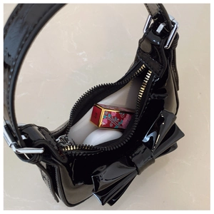 Détail intérieur du sac en cuir verni noir avec nœud, montrant l'espace pour rouge à lèvres