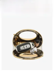 Detail showing high-gloss gold crescent bag with transparent acrylic side and inner storage