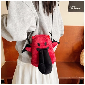 Détail du sac bandoulière monstre en peluche rouge avec ailes noires sur un banc en bois