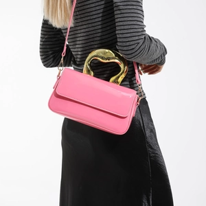 Pink glossy patent leather crossbody bag with a modern sculptural gold metal handle