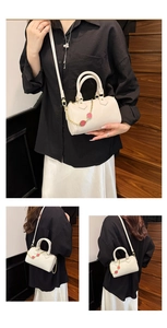 Detailed view of white Boston bag with red strawberry charms and golden hardware