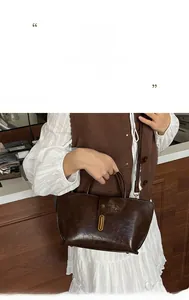 Detail of dark brown glossy leather tote bag with gold oval buckle and retro top handle