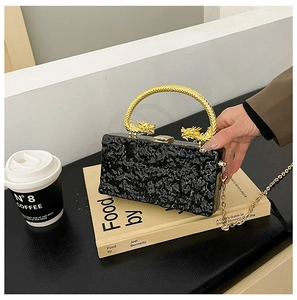 Detail of black pleated acrylic clutch featuring unique golden dragon-shaped handle