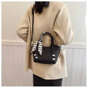 Detail of black pebbled leather bucket bag with houndstooth silk scarf on white coat