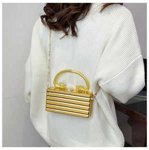 Detail of gold acrylic clutch with dragon head handles and ribbed texture on white knit