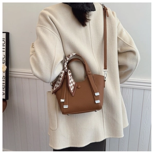 Detail view of brown pebbled leather bucket bag with a patterned silk scarf on the handle