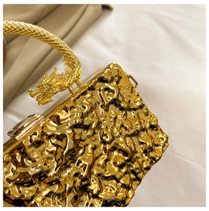 Close-up of golden acrylic clutch bag with crinkled texture and dragon-shaped top handle