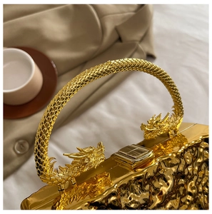 Detailed view of an ornate gold dragon handle on a metallic textured evening handbag