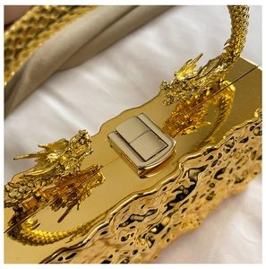 Detail of a luxury gold acrylic evening clutch featuring dual dragon heads and hammered texture