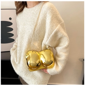 Detail of artistic gold torso-shaped crossbody bag with polished mirror finish and chain