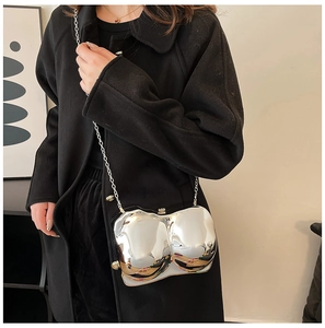 Close-up of silver mirror-finish bra-shaped bag with metal chain on a black coat