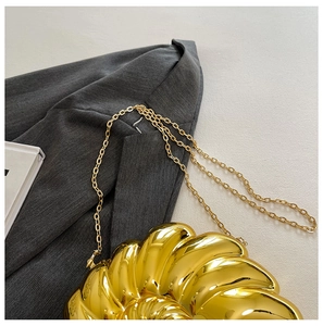 Detailed shot of a metallic gold shell-shaped clutch with a spiral texture on a grey blazer