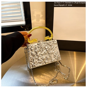 Detail of silver evening clutch with hammer texture and golden dragon-head handle