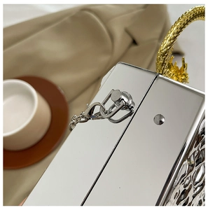 Detail of silver acrylic clutch box featuring an ornate golden dragon-shaped top handle