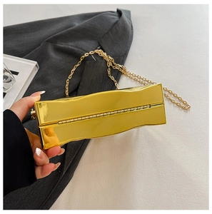 Dettaglio della pochette in acrilico dorato con trama a onde e catena in metallo sottile