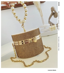 Detailed view of the gold cylindrical evening bag with rhinestones and pearl handle