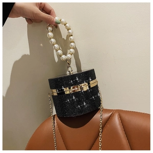 Detail of black cylindrical evening bag with rhinestones, pearl handle and gold chain strap