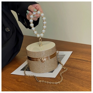 Detail of golden rhinestone cylindrical bag with pearl handle on a wooden table