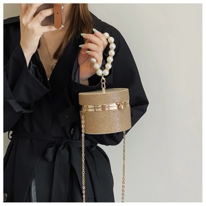Chic cylindrical evening bag with rhinestones and pearl handle worn by a model