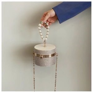 Close-up of sparkling rhinestone cylinder bag with pearl handle and golden chain