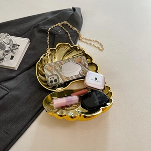 Elegant gold shell evening bag with acrylic chain and metallic finish on a grey suit