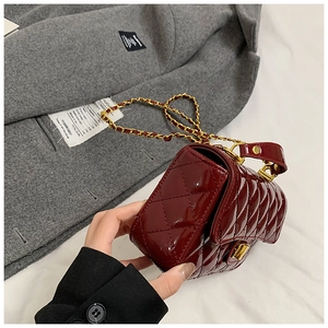 Detailed macro view of deep red patent leather mini bag with gold chain and turn lock