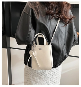Detail of cream leather handbag with metallic logo and heart ribbon charm accessory