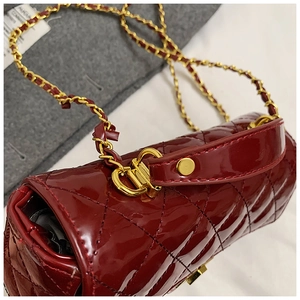 Macro shot of burgundy glossy patent leather with quilted texture and gold chain strap