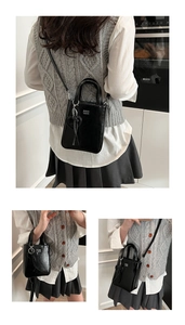 Detail of black glossy square handbag with letter embossing and heart charm attachment