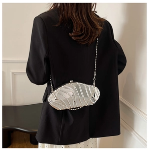 Detail of silver shell-shaped evening bag with metallic wave texture on model