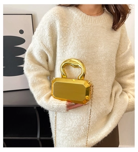 Detail van een geometrische gouden acryl clutch met een stevig handvat en metalen ketting