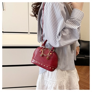Burgundy shell bag with gold rivets and chain pendant worn by model in casual style
