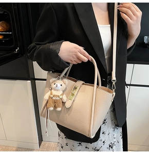 Dettaglio borsa a secchiello in pelle beige con chiusura dorata e ciondolo orsetto
