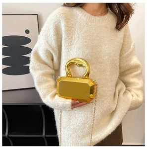 Detail van een gouden achthoekige avondtas van acryl met dikke metalen handgreep en ketting