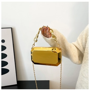 Detail van goudkleurige acryl clutch met geometrische vlakken en dikke gouden ketting