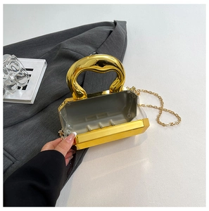 Detail van gouden avondtas met rond metalen handvat en fijne gouden kettingriem