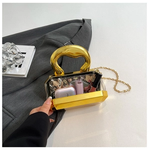 Detail van acryl avondtas met gouden metalen handvat en ketting op een kostuumjas