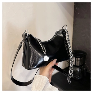 Detail of black glossy leather handbag with bold silver chain and metal tag pendant