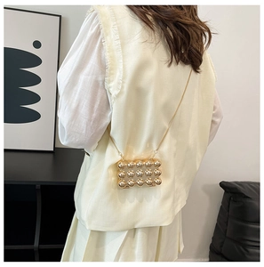 Close-up of mini gold metallic crossbody bag with beaded texture worn over the shoulder