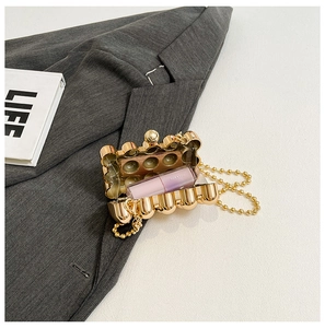 Detail of gold mini evening bag with wavy texture and beaded chain holding a lipstick