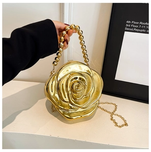 Detail of a golden rose-shaped evening clutch bag with beaded handle and metal chain strap