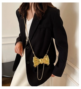 Close-up of golden metallic bow-shaped mini crossbody bag with sleek bead chain