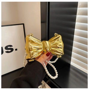 Close-up of golden bow-shaped metal mini bag with elegant pearl chain strap detail