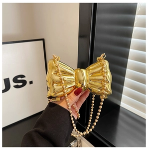 Macro detail of golden bow-shaped hard shell evening bag with detachable bead chain strap