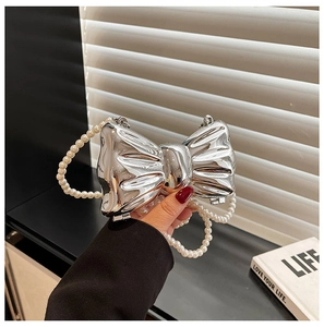 Macro detail of silver bow-shaped metal evening bag with elegant pearl chain strap
